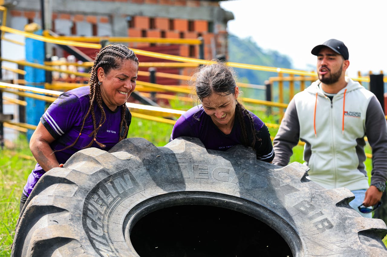 Two women and a man engage in an outdoor fitness session flipping a large tire.