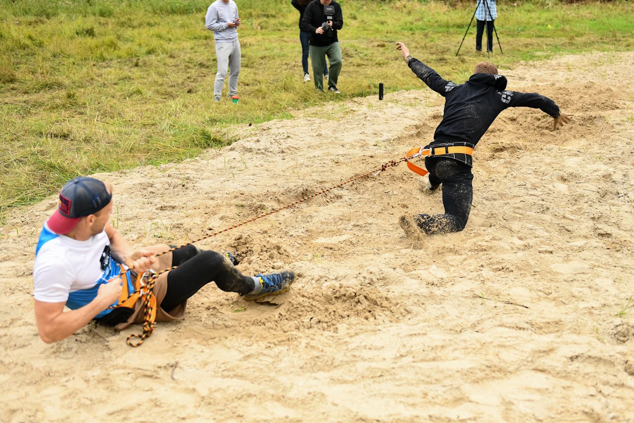Men participating in a competitive team-building event, pulling ropes in the sand.